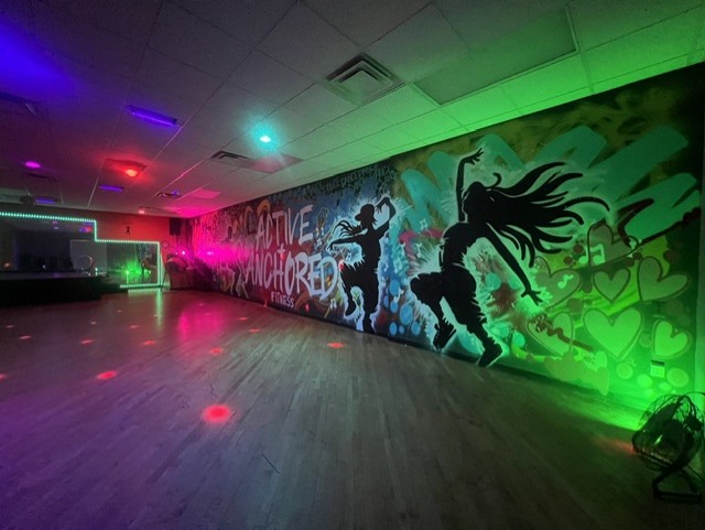 Active + Anchored studio floor lit in purple, pink and green with the signature graffiti mural wall